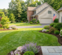 Professionally landscaped suburban lawn in Clarence, NY, with a detailed model train layout featuring a miniature factory and town nestled in native flowering beds (purple coneflowers, hydrangeas). Perfect example of a tailored, complex landscape design that local experts can build.
