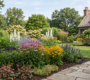A professionally landscaped estate garden in Clarence New York featuring tiered perennial borders with purple coneflowers, black-eyed susans, and lush green hostas along a natural stone flagstone walkway.